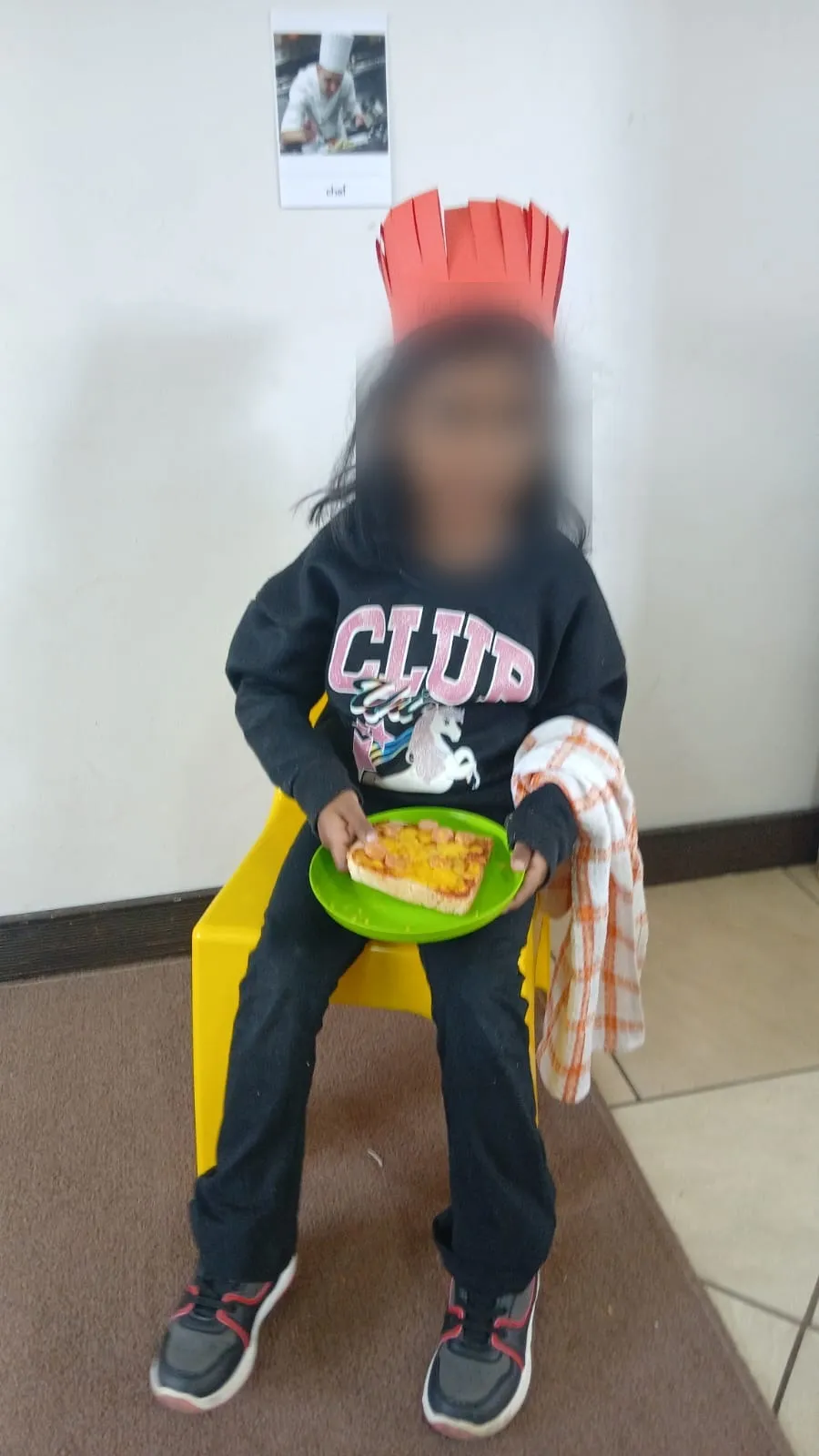 A seated little chef with her toasted pizza on a green plate