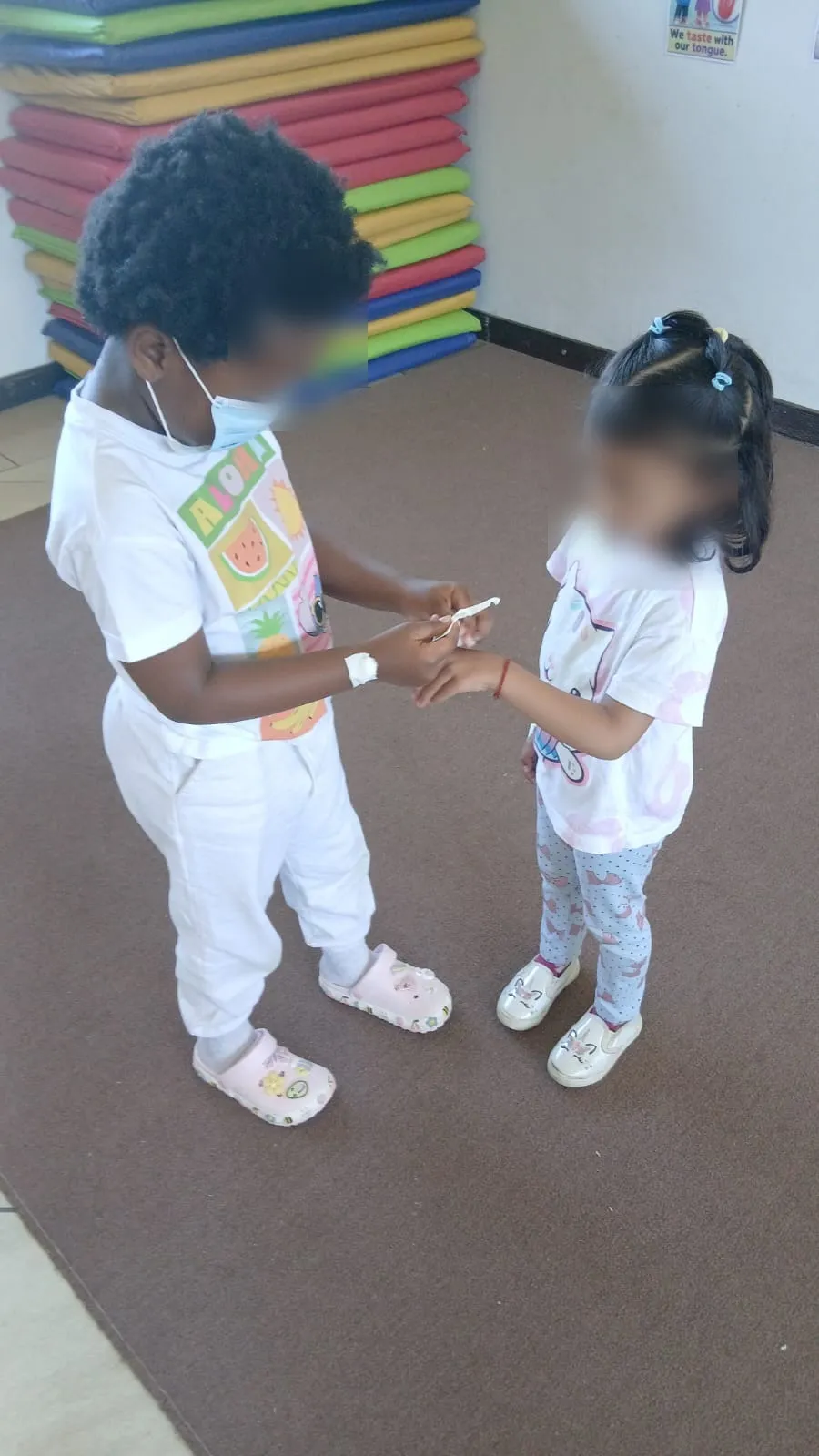 Two children playing doctor, one wrapping a bandage around the other's wrist